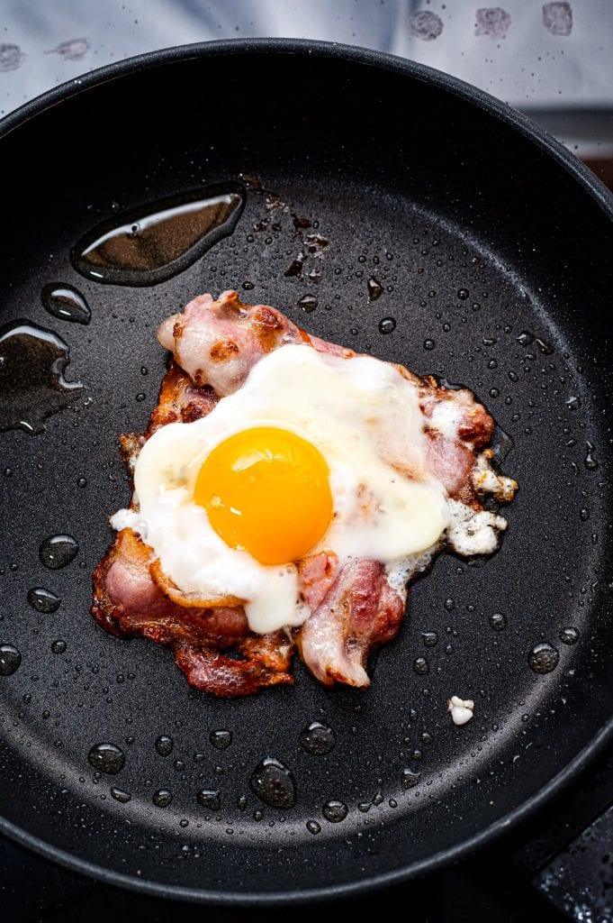 Frying pan with bacon making a shape of a square and a fried egg in the center.