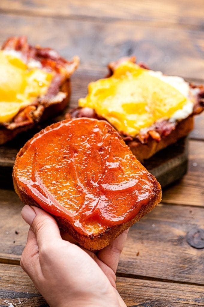 Hand holding a piece of toast with ketchup spread on it.