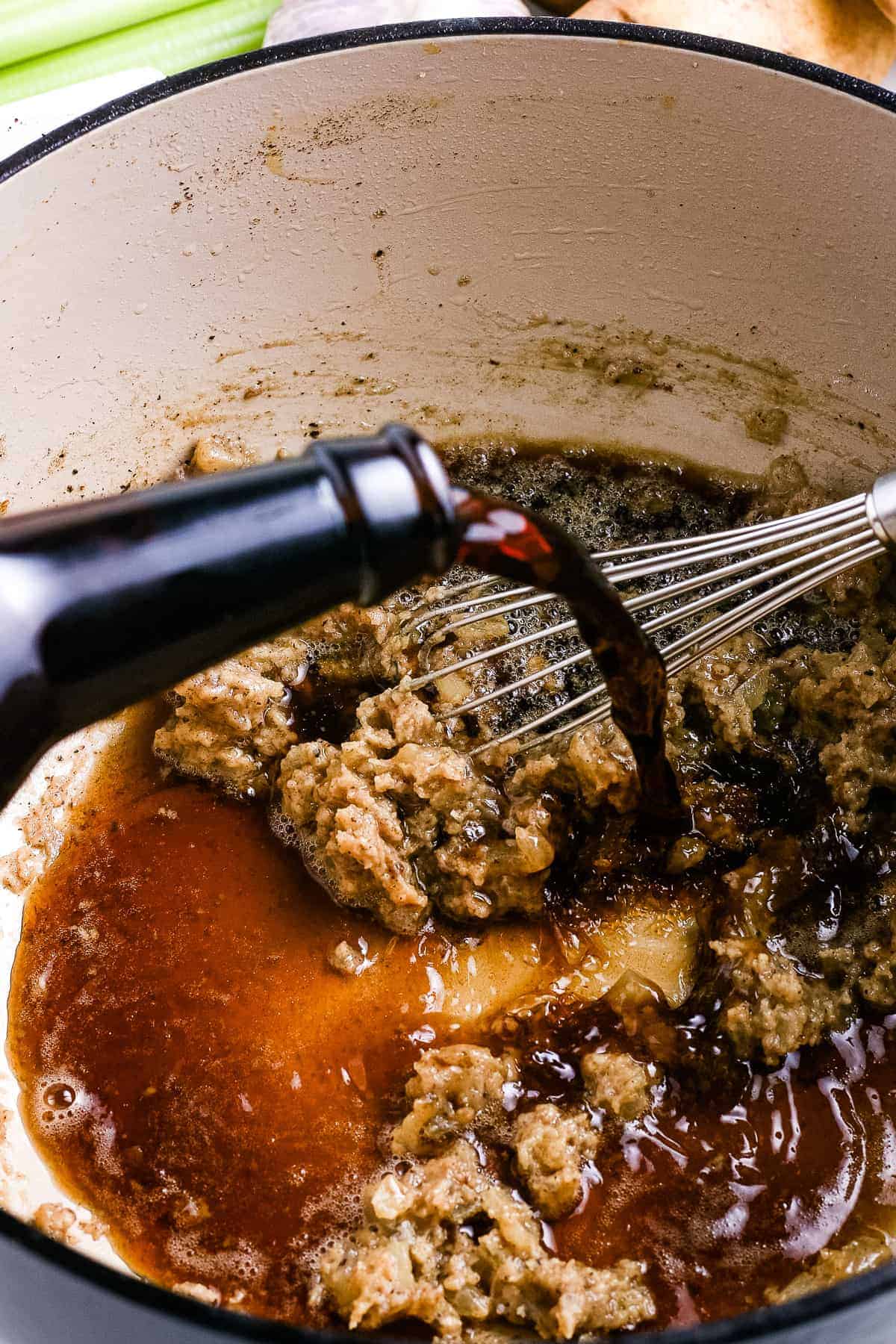 Guinness beer being poured into roux in white dutch oven