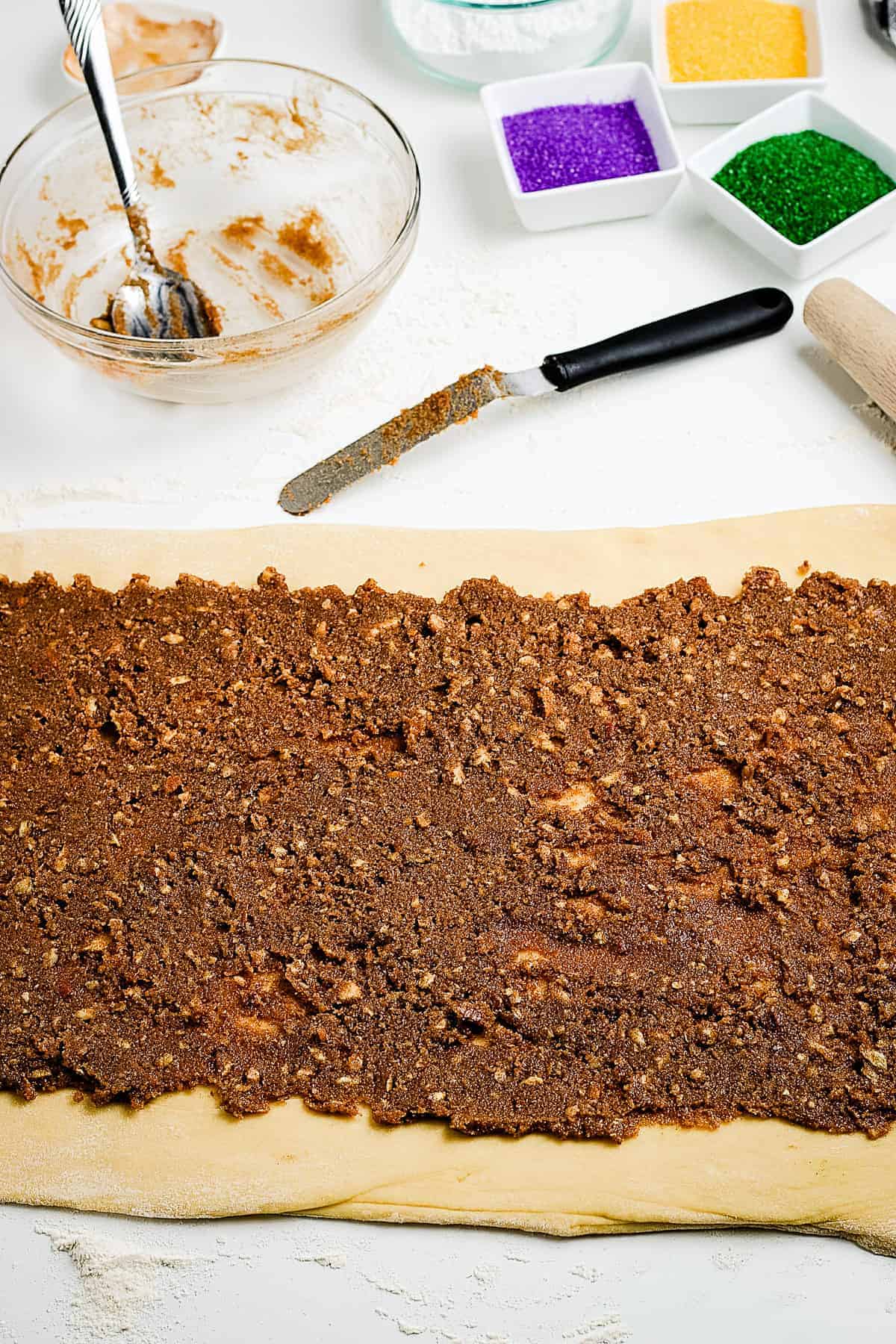 Dough in a rectangle and topped with cinnamon sugar and pecans.