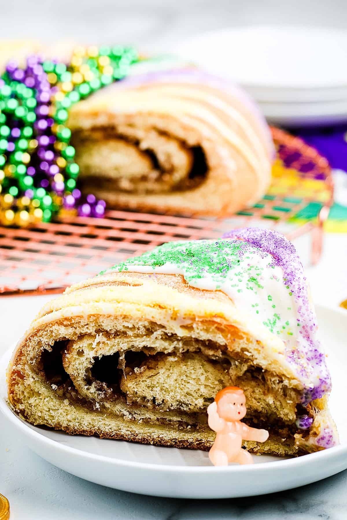 Slice of King Cake on a white plate with plastic baby