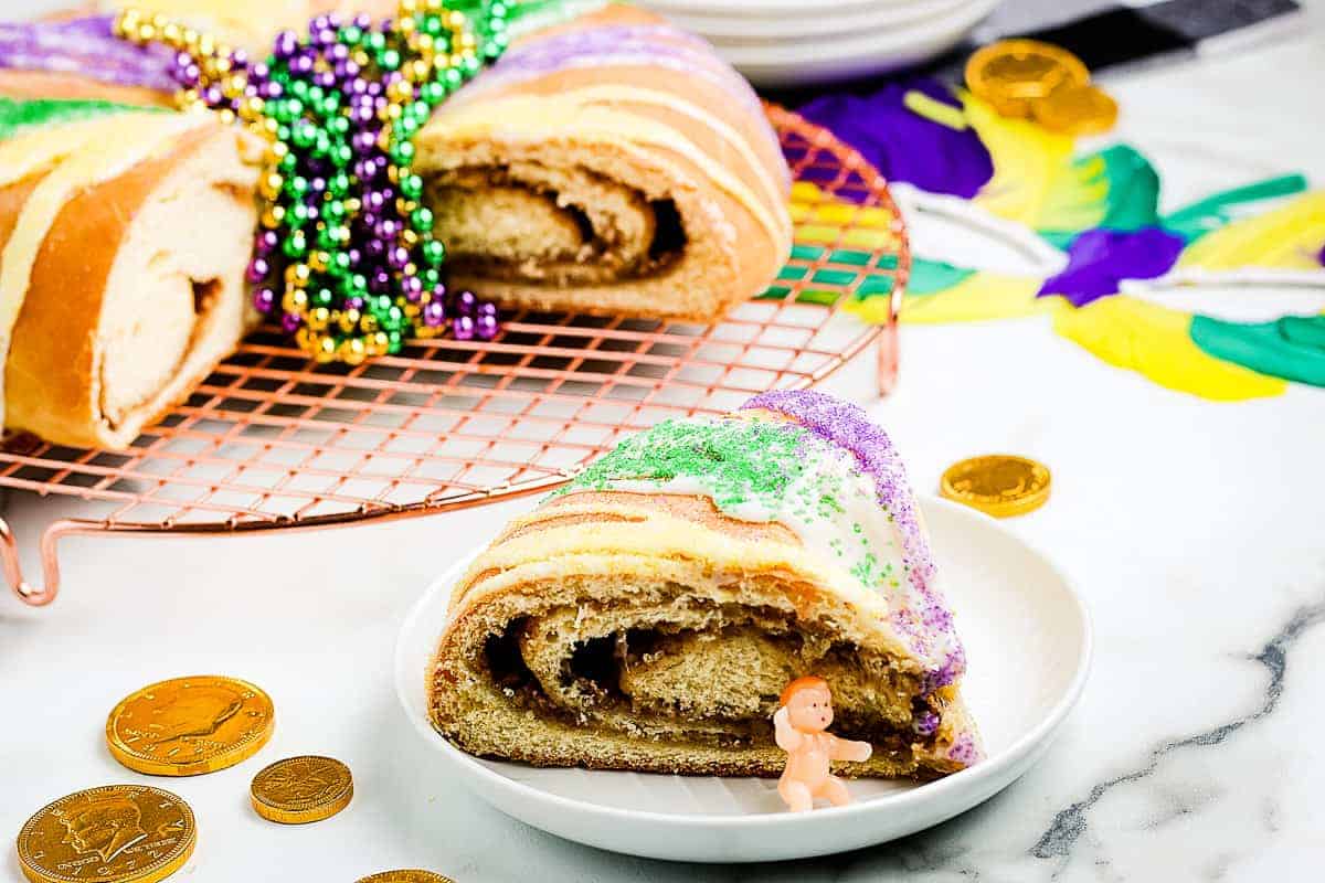 King Cake slice on white plate with full cake behind it