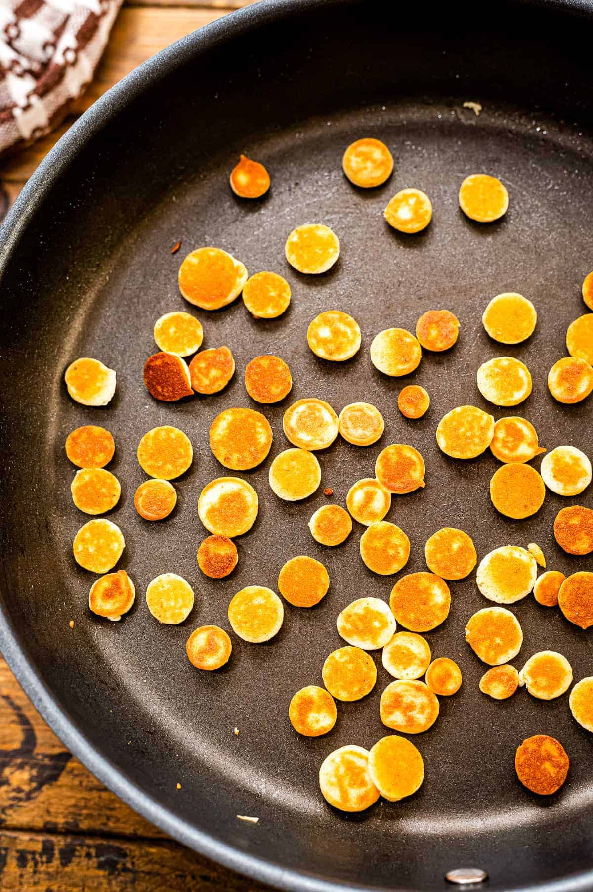 Skillet with browned mini pancakes in it