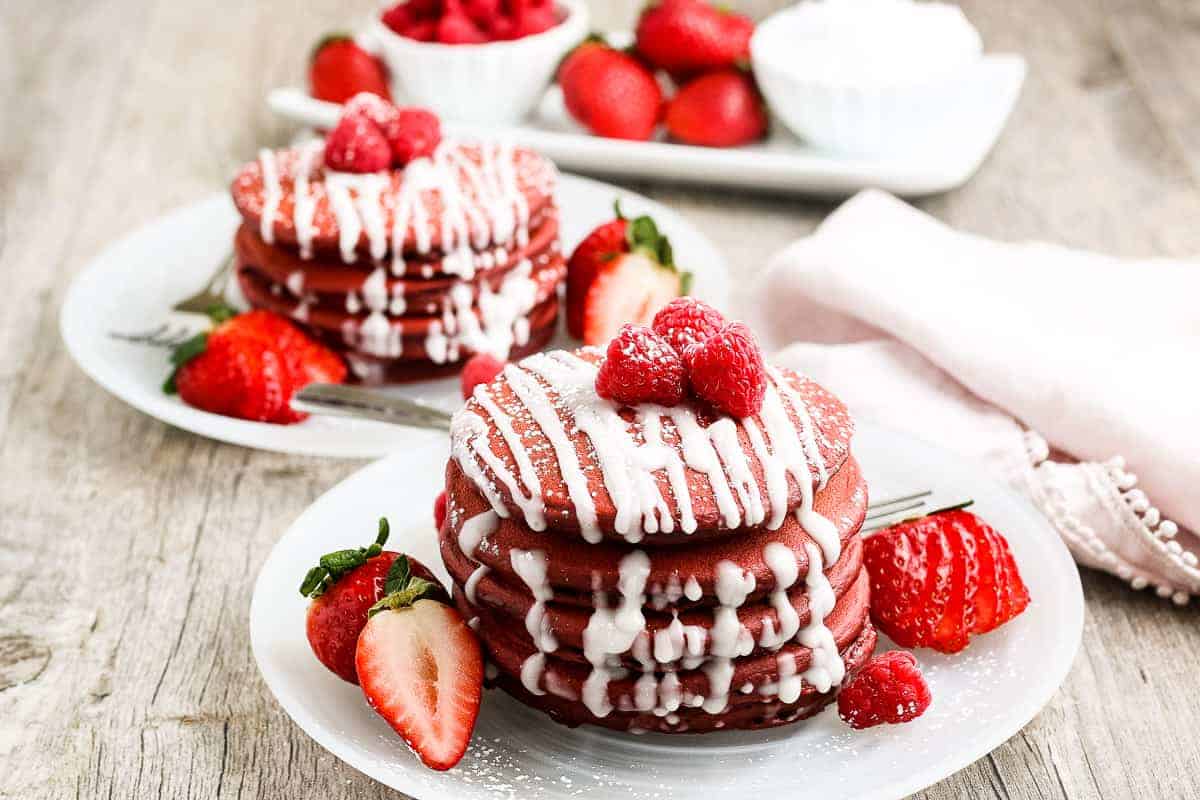 Red Velvet Pancakes stacked with a cream cheese drizzle on a white plate
