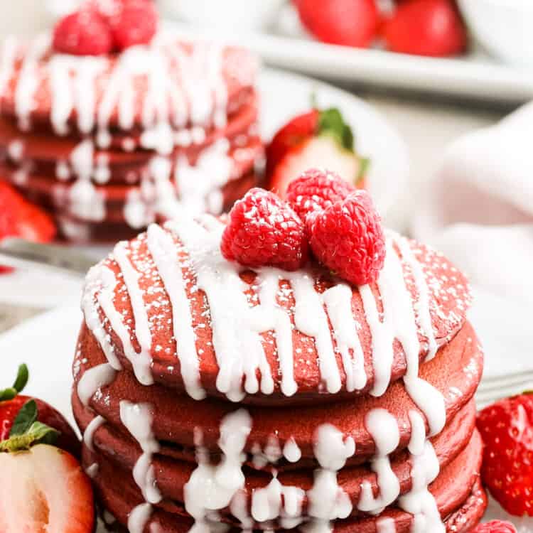 Stack of red velvet pancakes with cream cheese drizzle on white plate