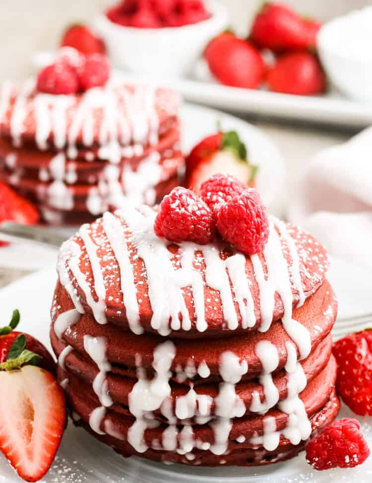 Stack of red velvet pancakes with cream cheese drizzle on white plate