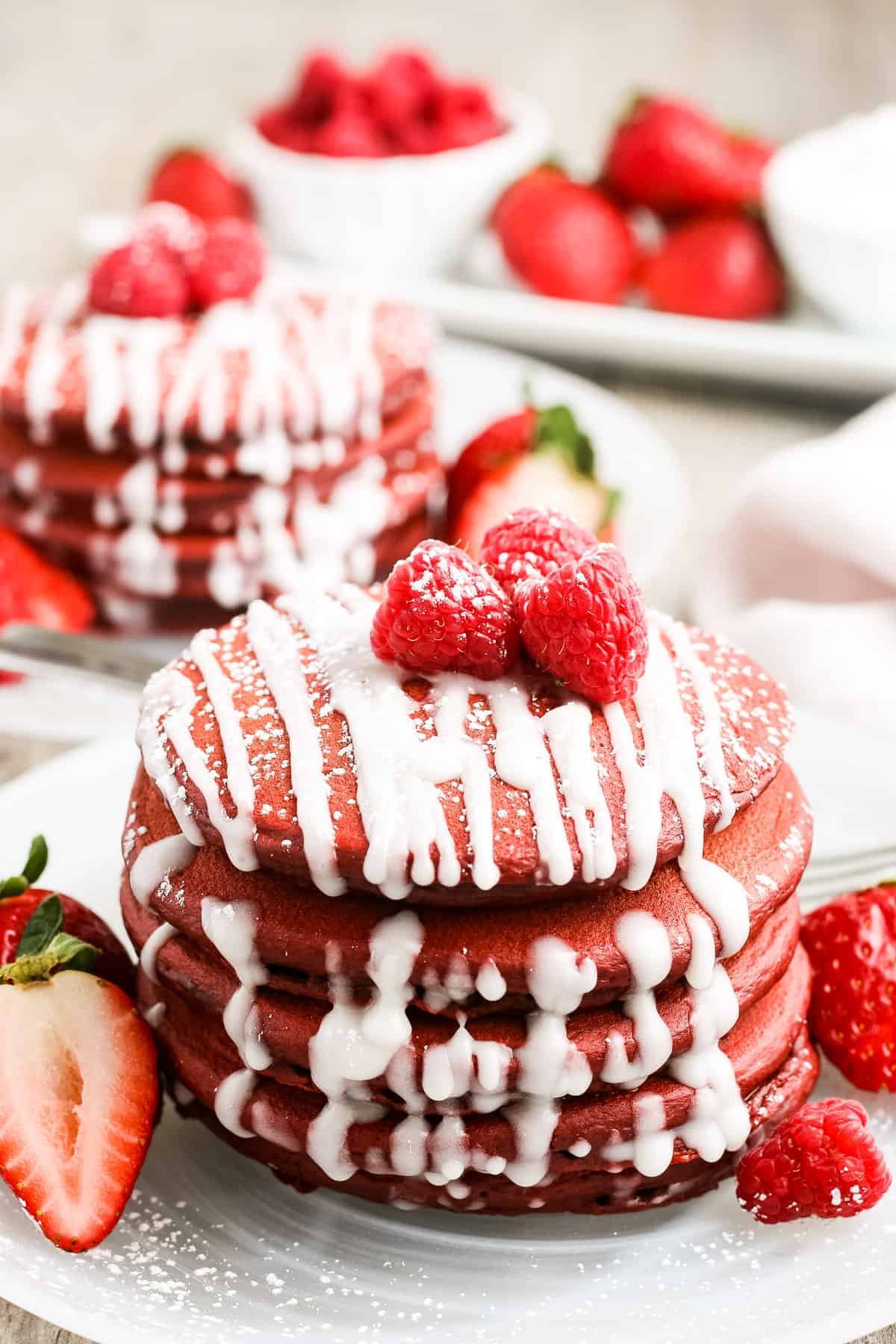 Stack of red velvet pancakes with cream cheese drizzle on white plate