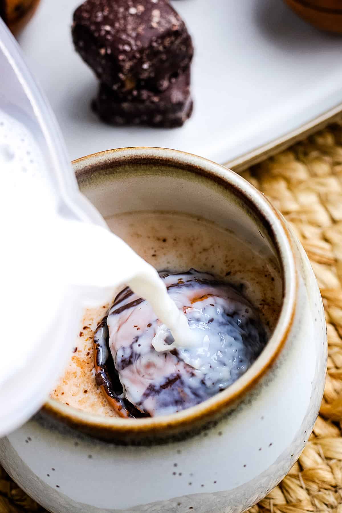 Hot milk being poured into a mug with salted caramel hot cocoa bomb