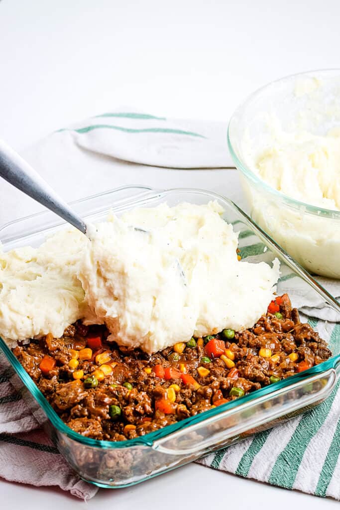 Spreading mashed potatoes on ground beef mixture in glass baking dish