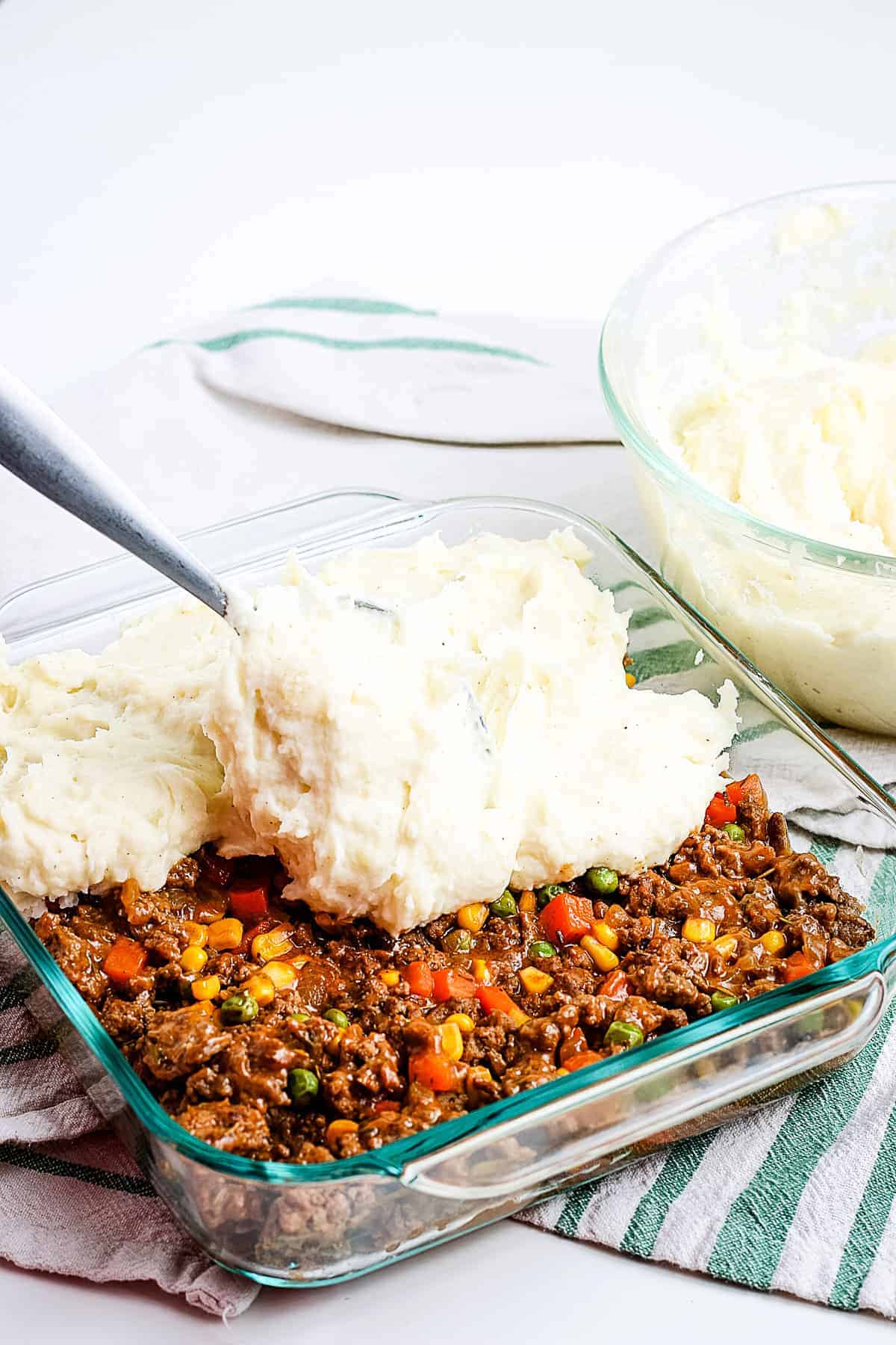 Spreading mashed potatoes on ground beef mixture in glass baking dish