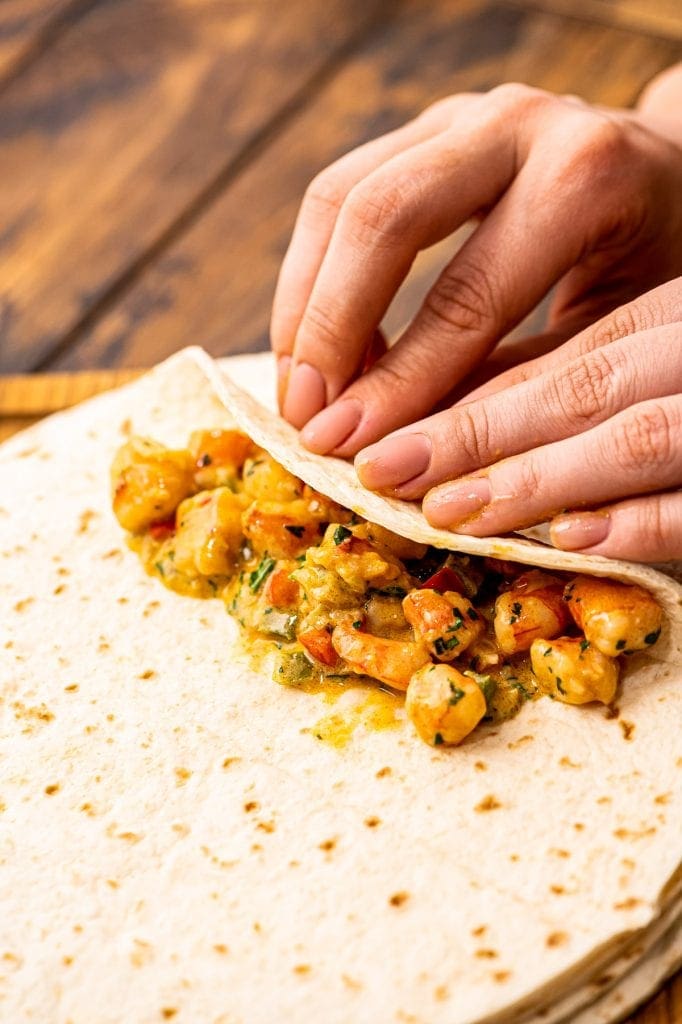 Hands rolling a tortilla filled with shrimp mixture.