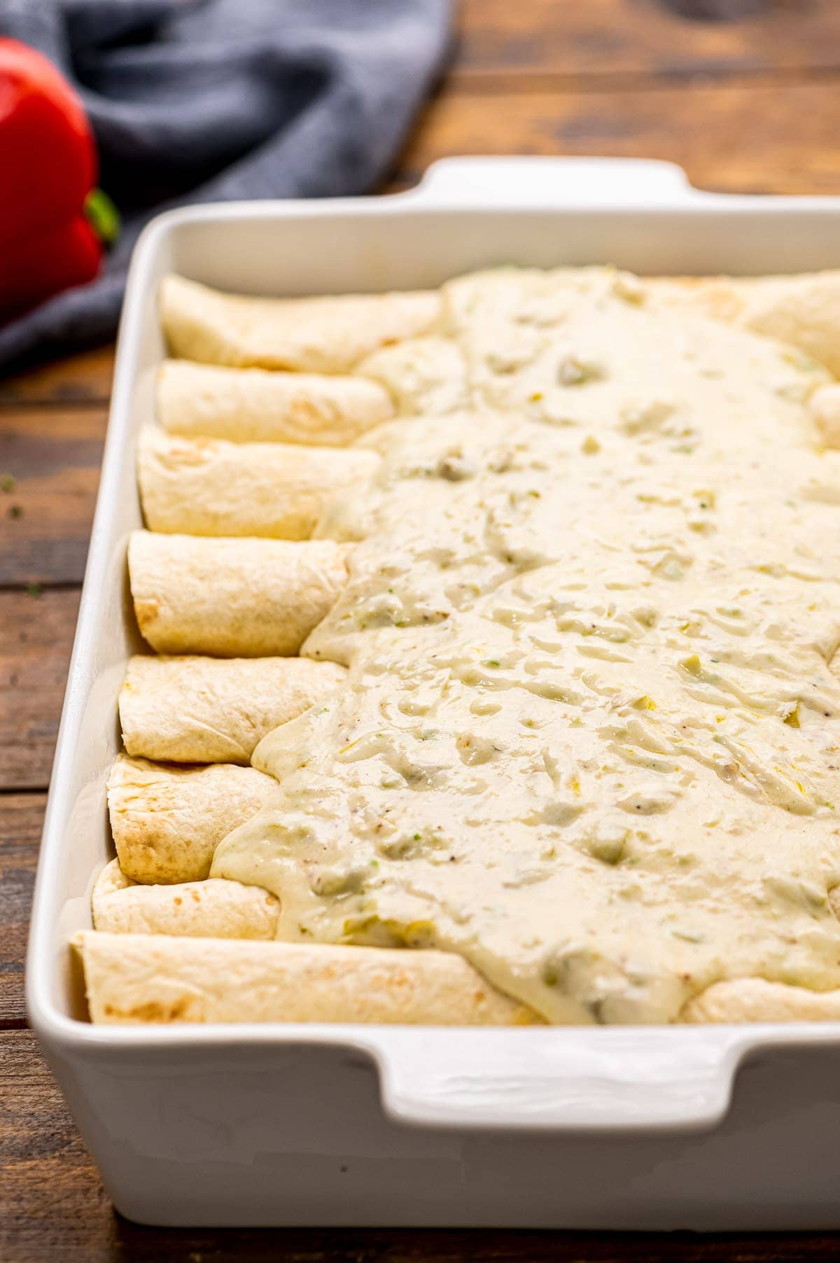 Enchiladas in white casserole dish with cream sauce poured on the top.