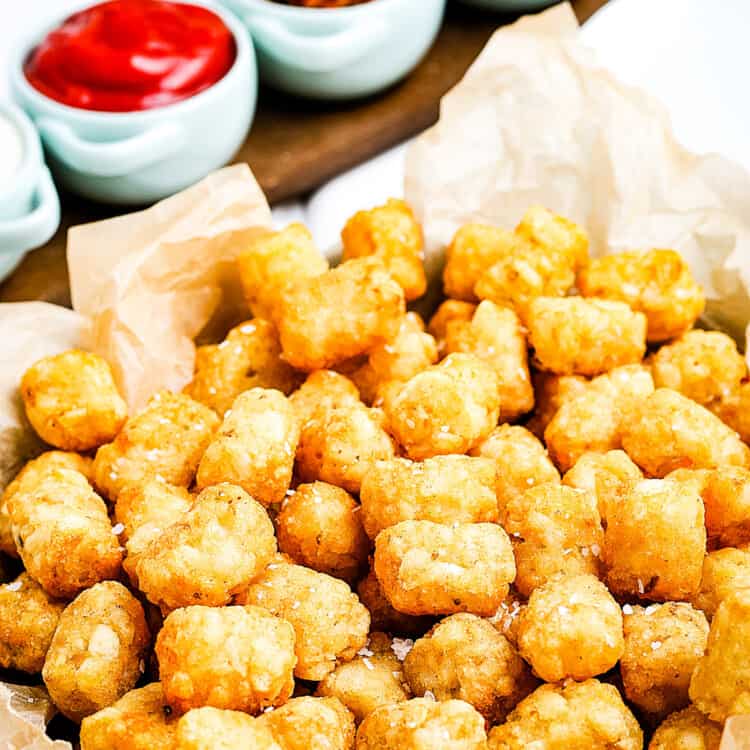 Air Fryer Tater Tots in a basket lined with brown paper and condiments behind