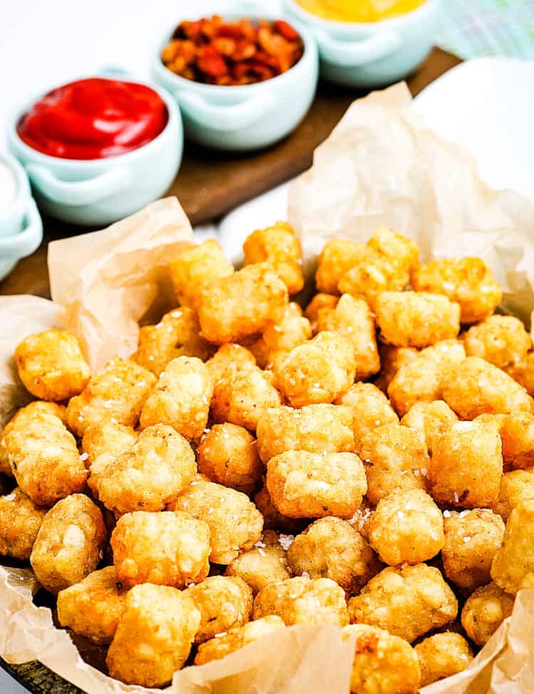 Air Fryer Tater Tots in a basket lined with brown paper and condiments behind