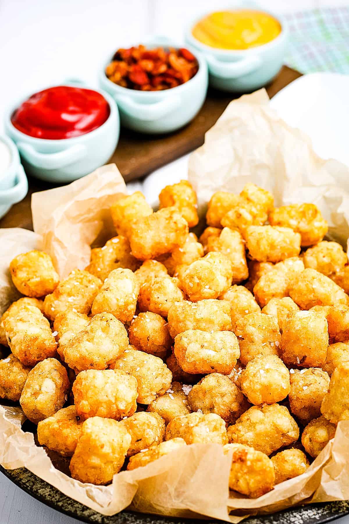 Air Fryer Tater Tots in a basket lined with brown paper and condiments behind