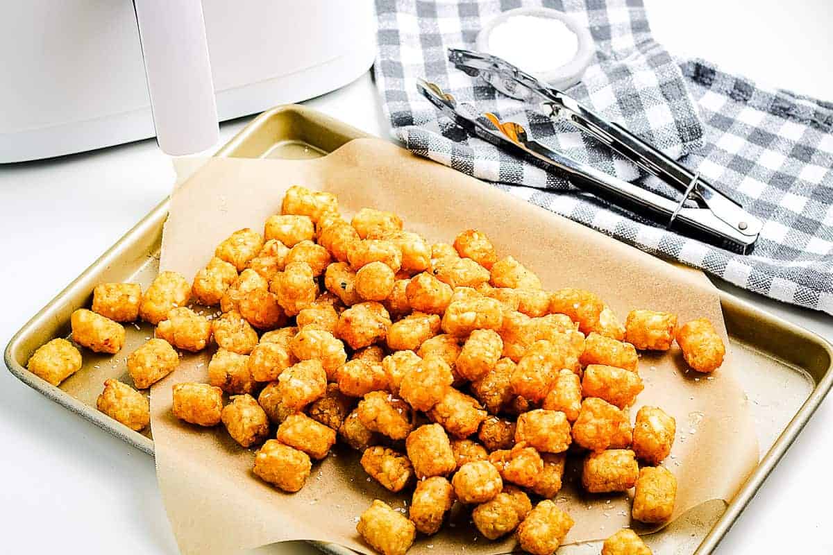 A sheet pan lined with brown paper with crispy tater tots on top