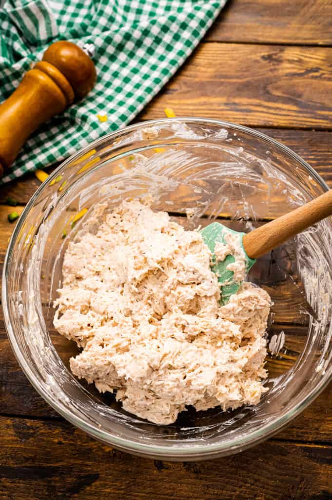 Mixing up cream cheese and chicken mixture with spatula in glass bowl