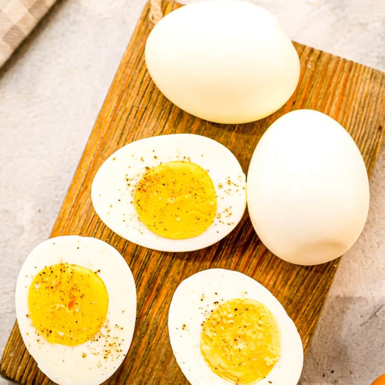 A brown wood cutting board with hard boiled eggs cut open with salt and pepper