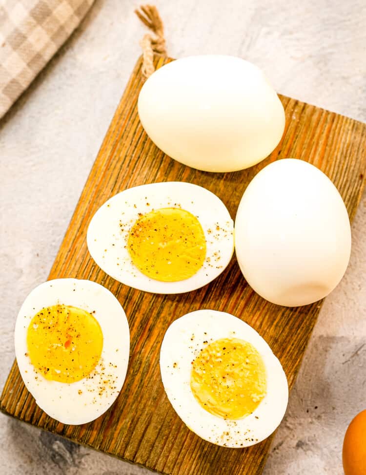 A brown wood cutting board with hard boiled eggs cut open with salt and pepper