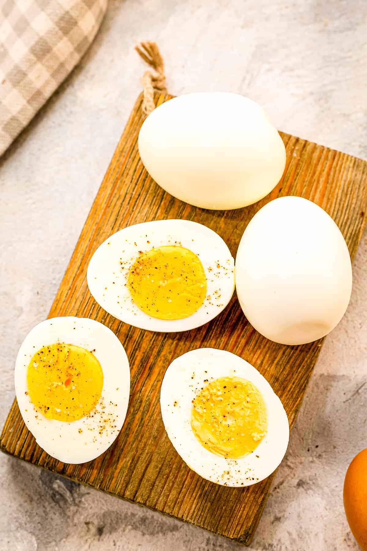 A brown wood cutting board with hard boiled eggs cut open with salt and pepper