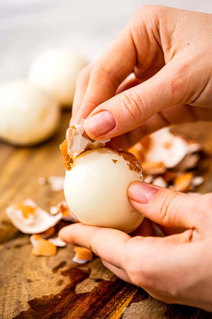 Hands peeling shell of brown hard boiled egg