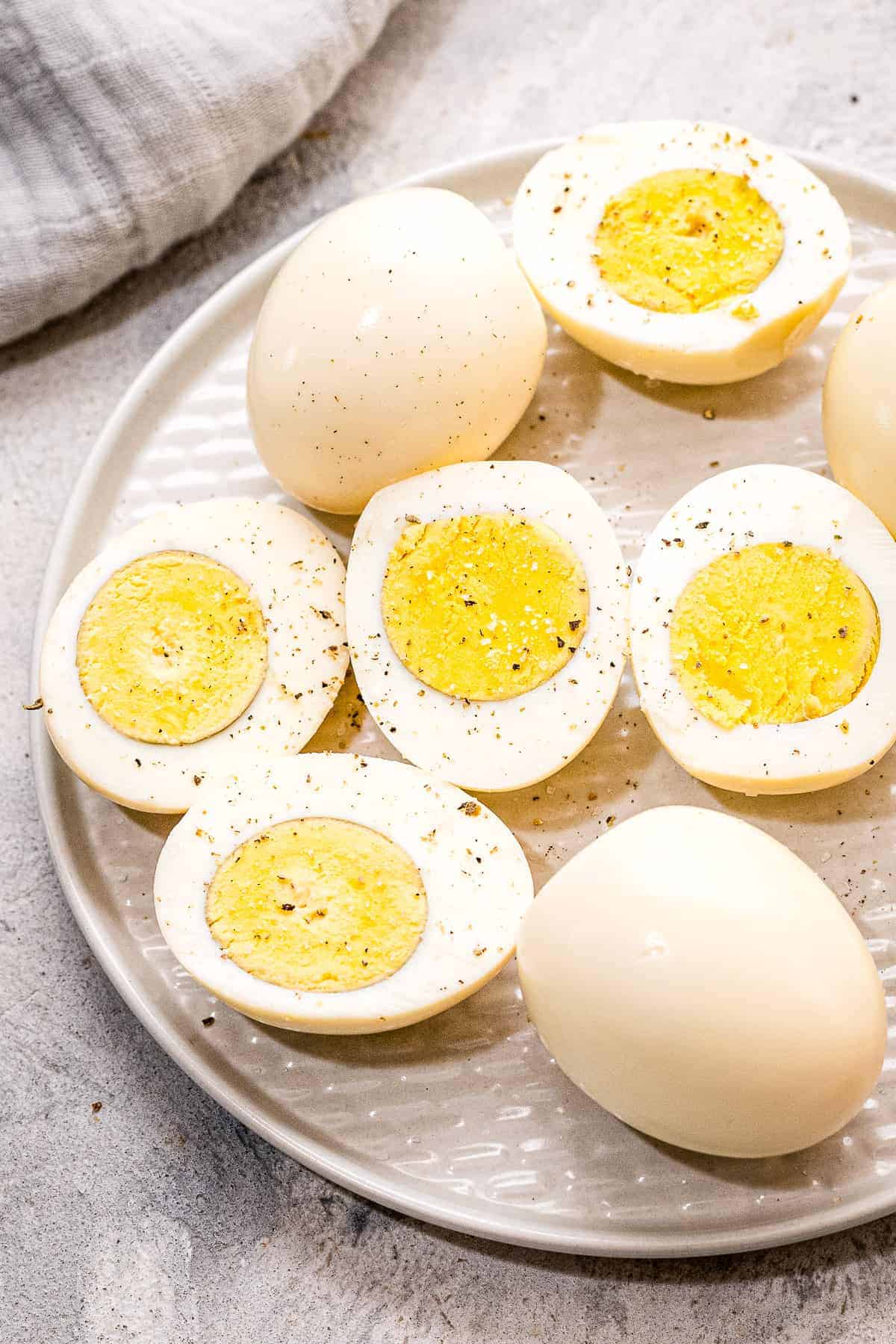 Hard Boiled Eggs with some cut in half on a plate and seasoned with pepper