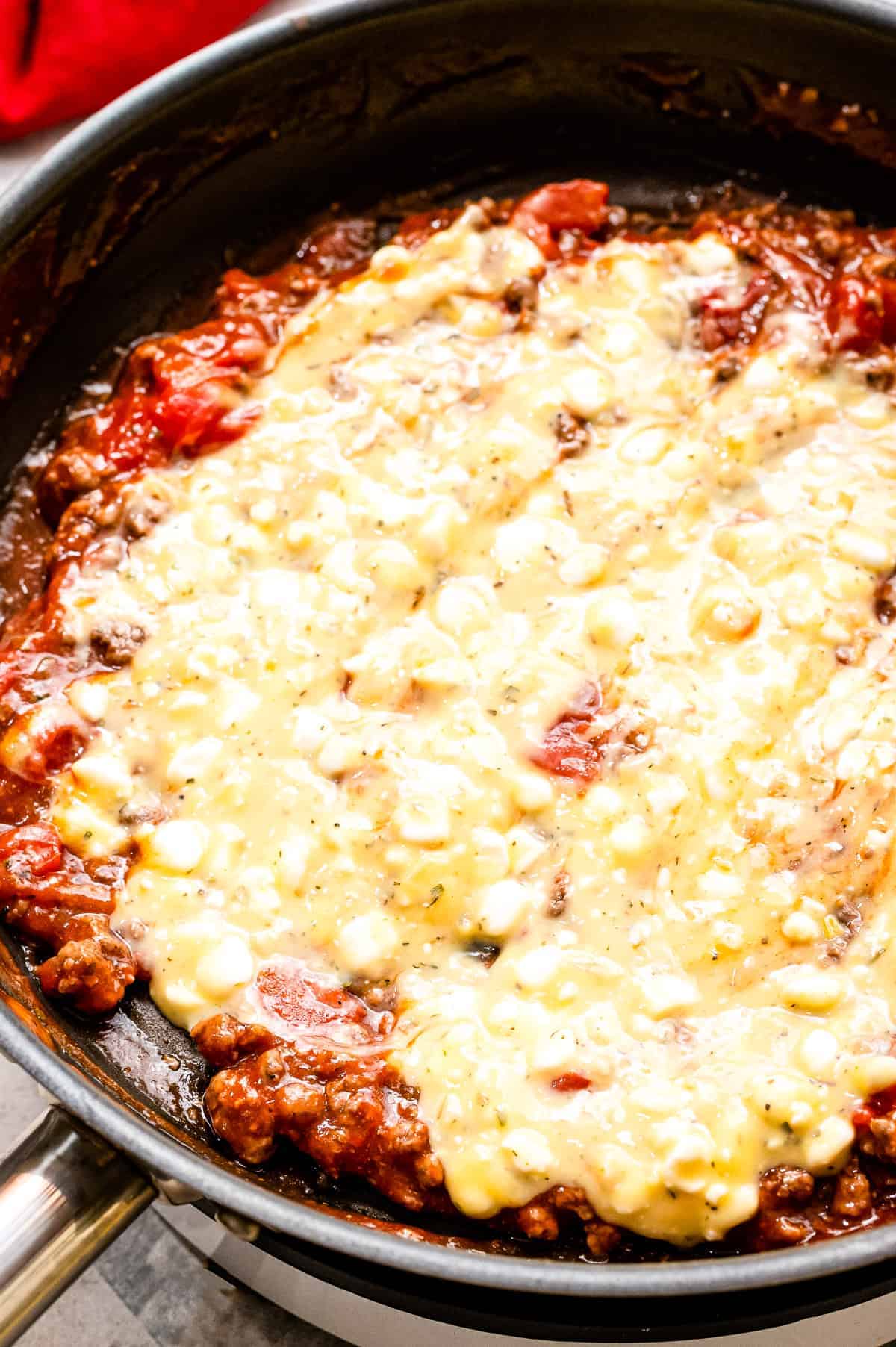 Layering cheese sauce on top of meat sauce in skillet