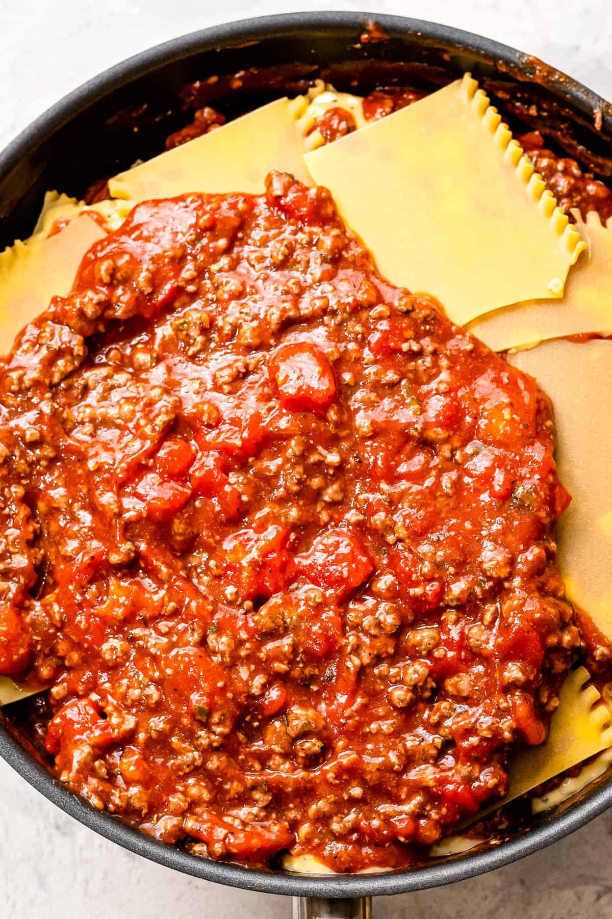 Topping lasagna noodles with meat sauce in skillet