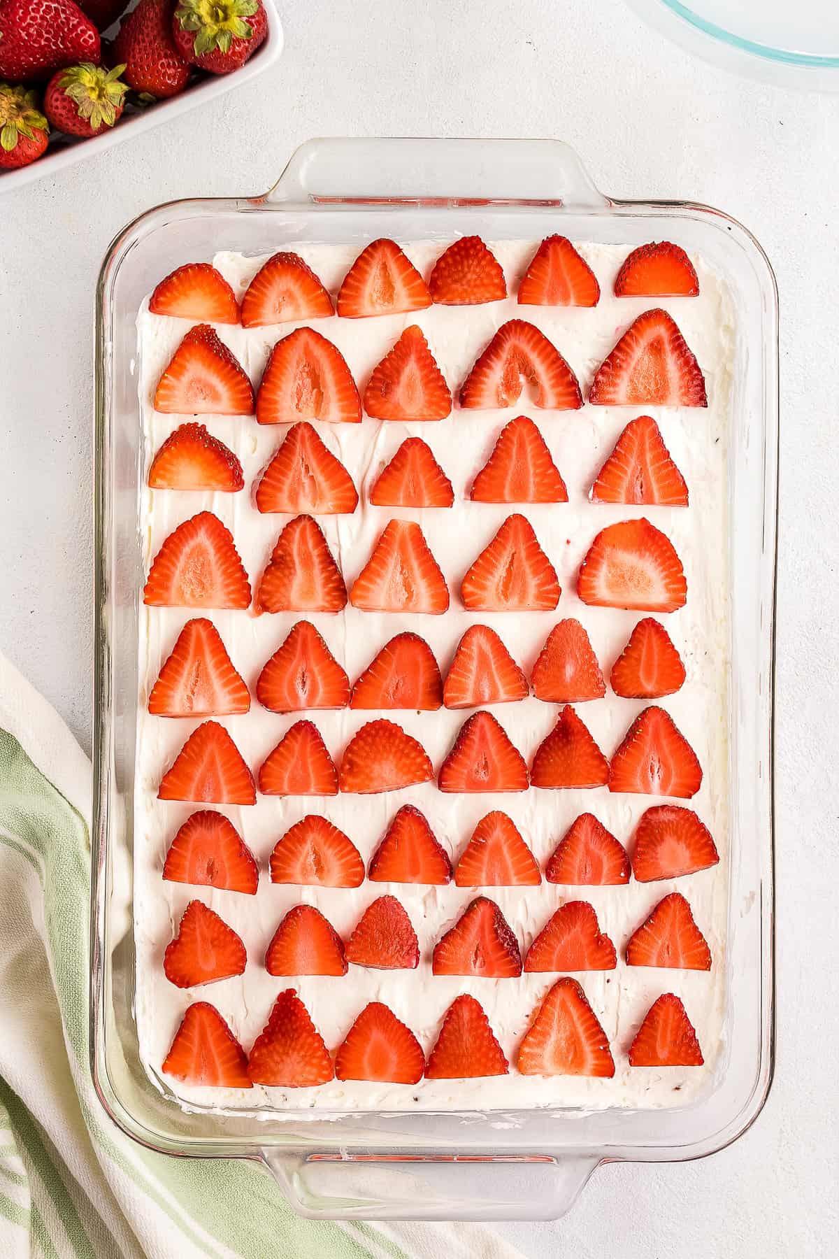 Sliced Strawberries on top of cream cheese layer in glass pan