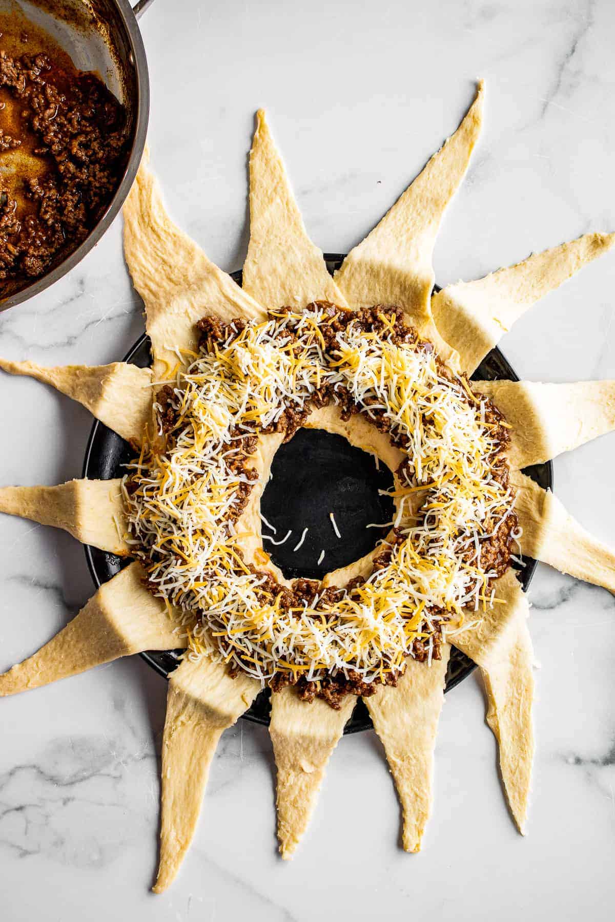 Crescent roll dough in ring filled with taco meat and cheese before folding dough over