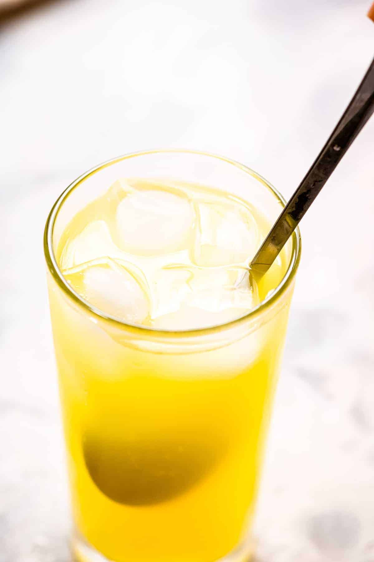 High ball glass with a spoon stirring orange juice and ice cubes