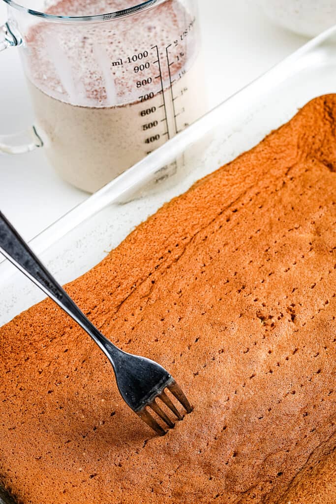 Fork Poking cake in a glass baking dish