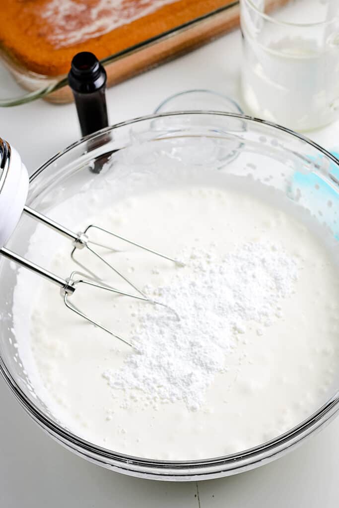 Powdered sugar being added to whipping cream in bowl