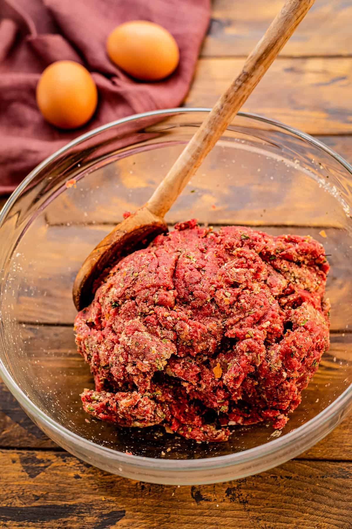A glass bowl with ground beef mixture for meatballs