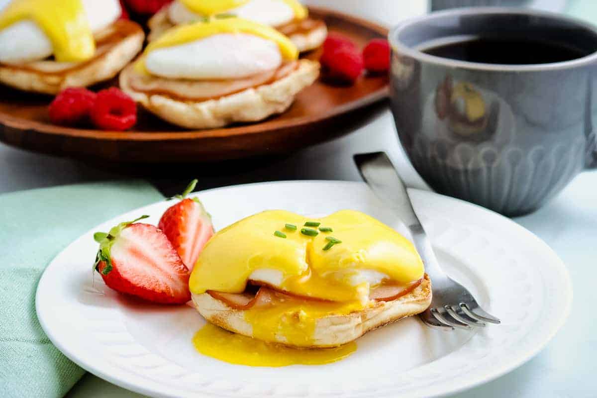 White plate with eggs benedict on it with fork next to it