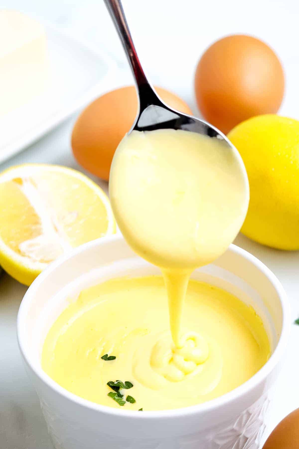 Spoon with Hollandaise Sauce on it over a bowl of sauce