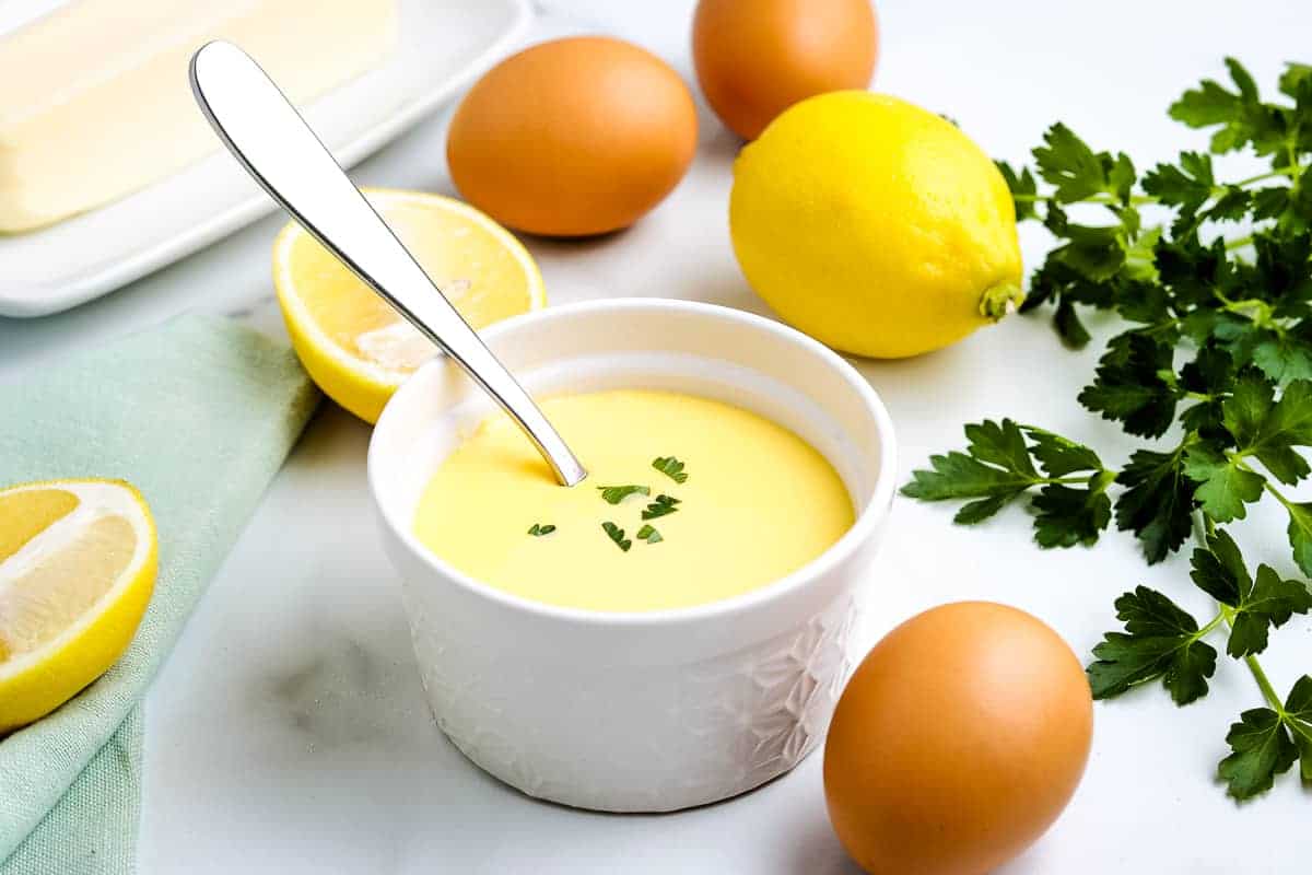A white ramekin with hollandaise and spoon in it