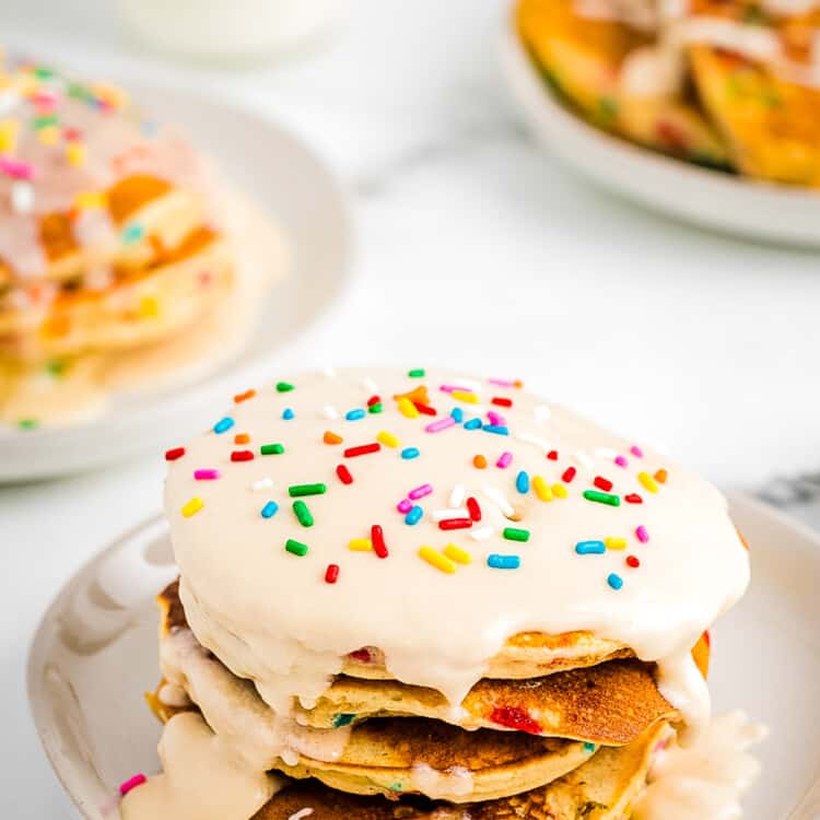 Stack of Funfetti Pancakes on plate topped with vanilla frosting and more sprinkles