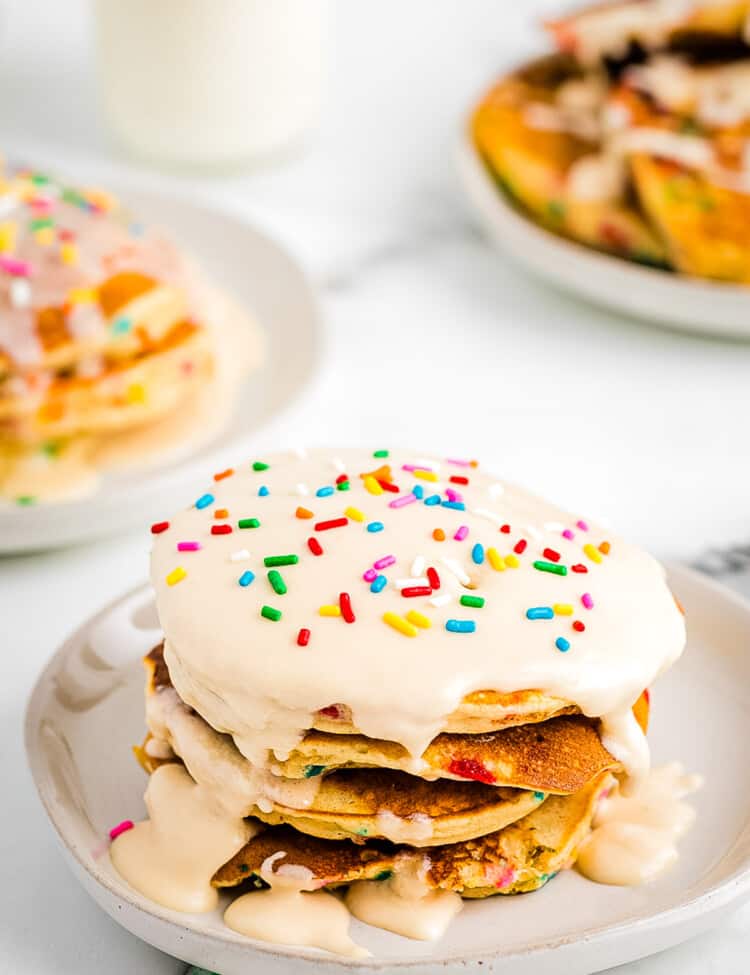 Stack of Funfetti Pancakes on plate topped with vanilla frosting and more sprinkles