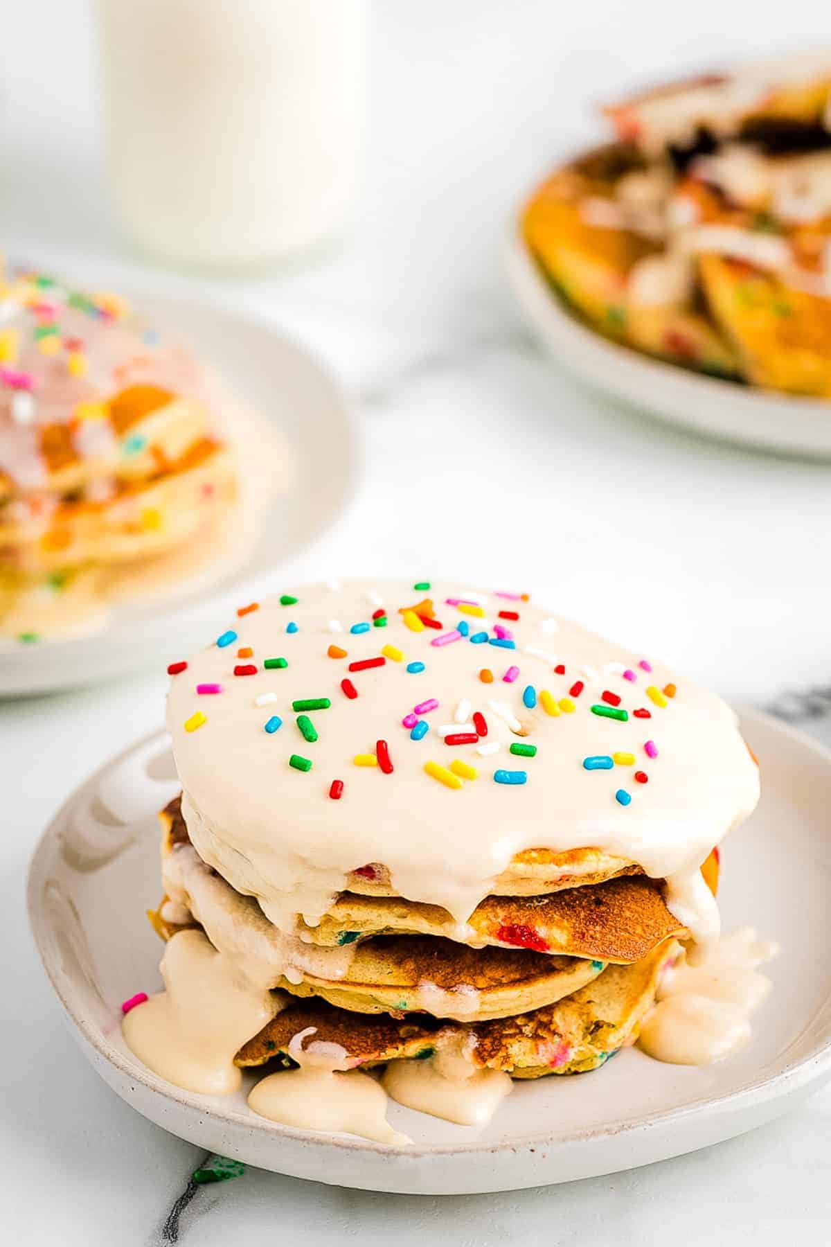 Stack of Funfetti Pancakes on plate topped with vanilla frosting and more sprinkles