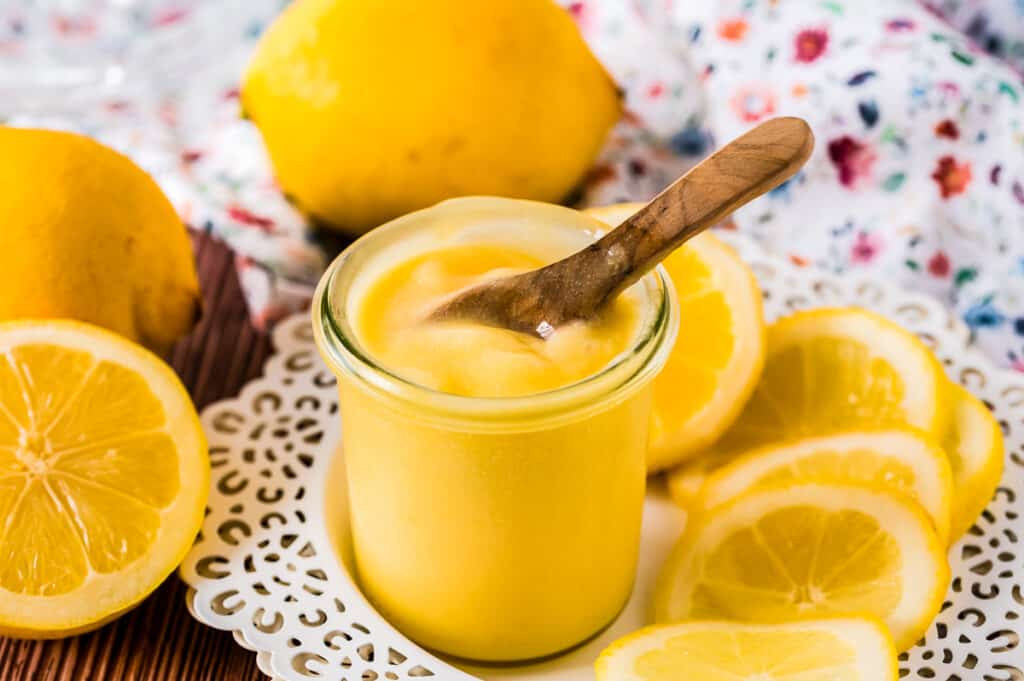 Small glass jar with lemon curd and a small wooden spoon in it