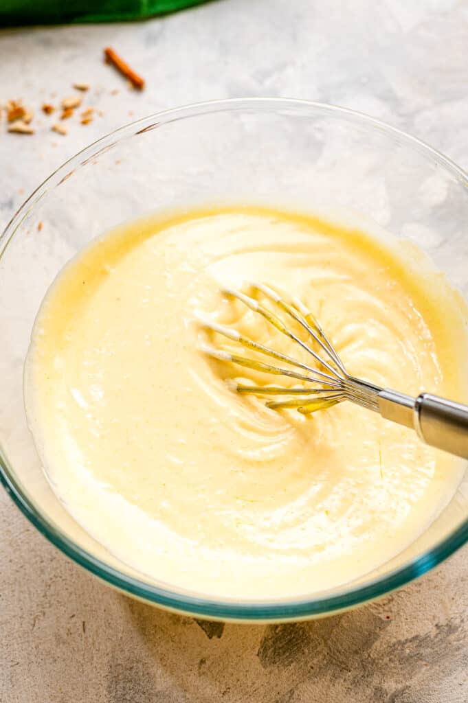 Glass bowl with whisk and ingredients in it to make pretzel dip after mixing