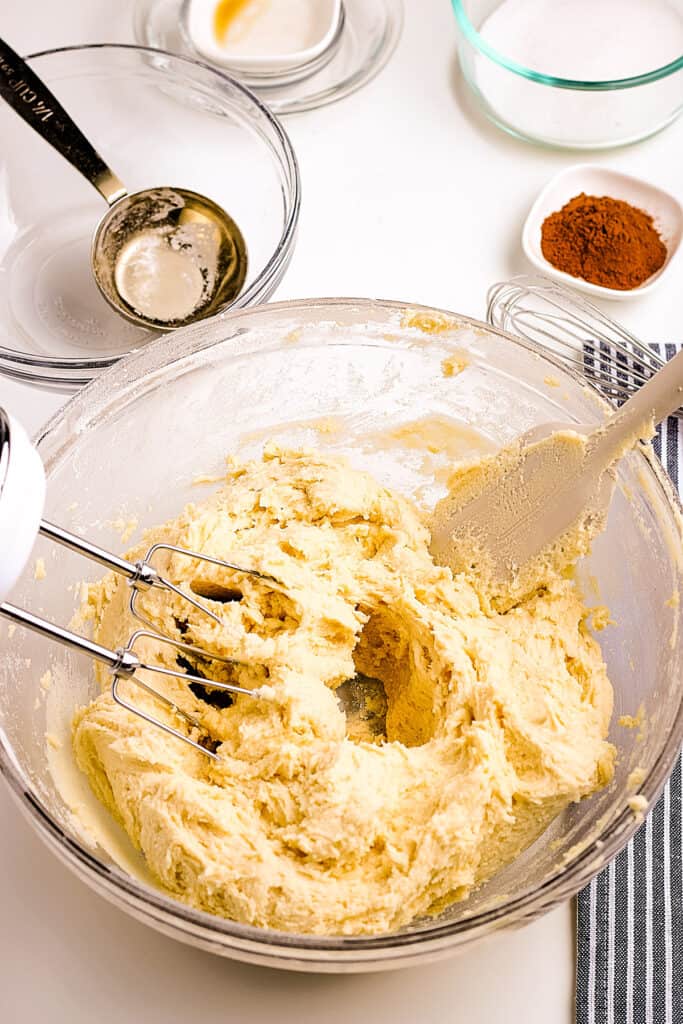 Bowl of cookie dough mixed together with hand beater sitting next to it