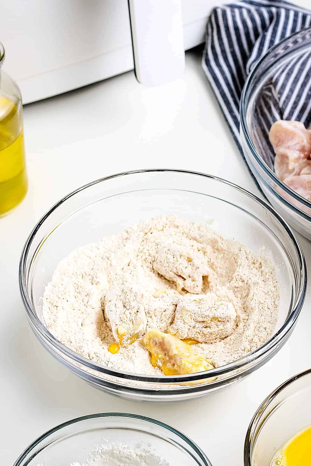 Chicken pieces being coated in a flour seasoning