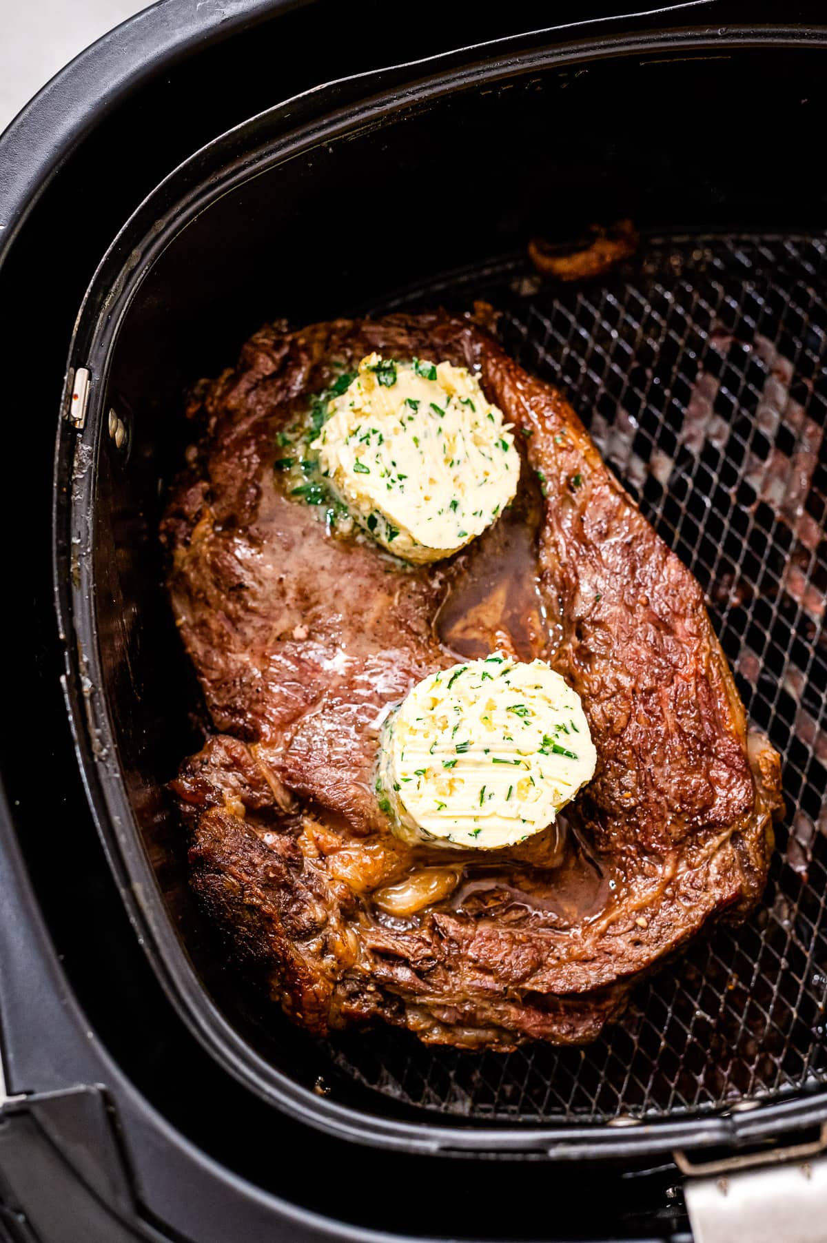 Air fryer basket with steak topped with garlic butter