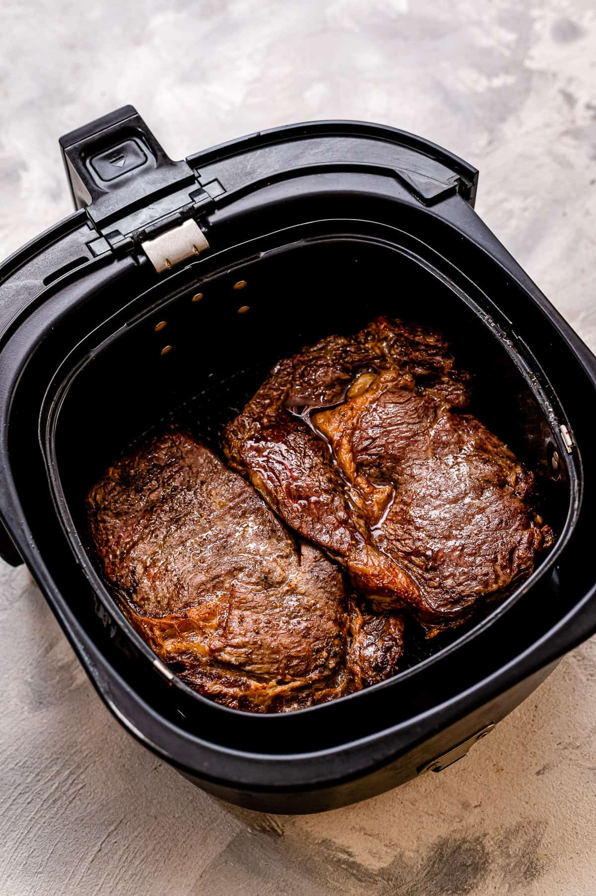 Air Fryer basked with cooked steaks in it