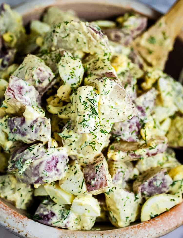Bowl of Dill Potato Salad with wooden spoon in it