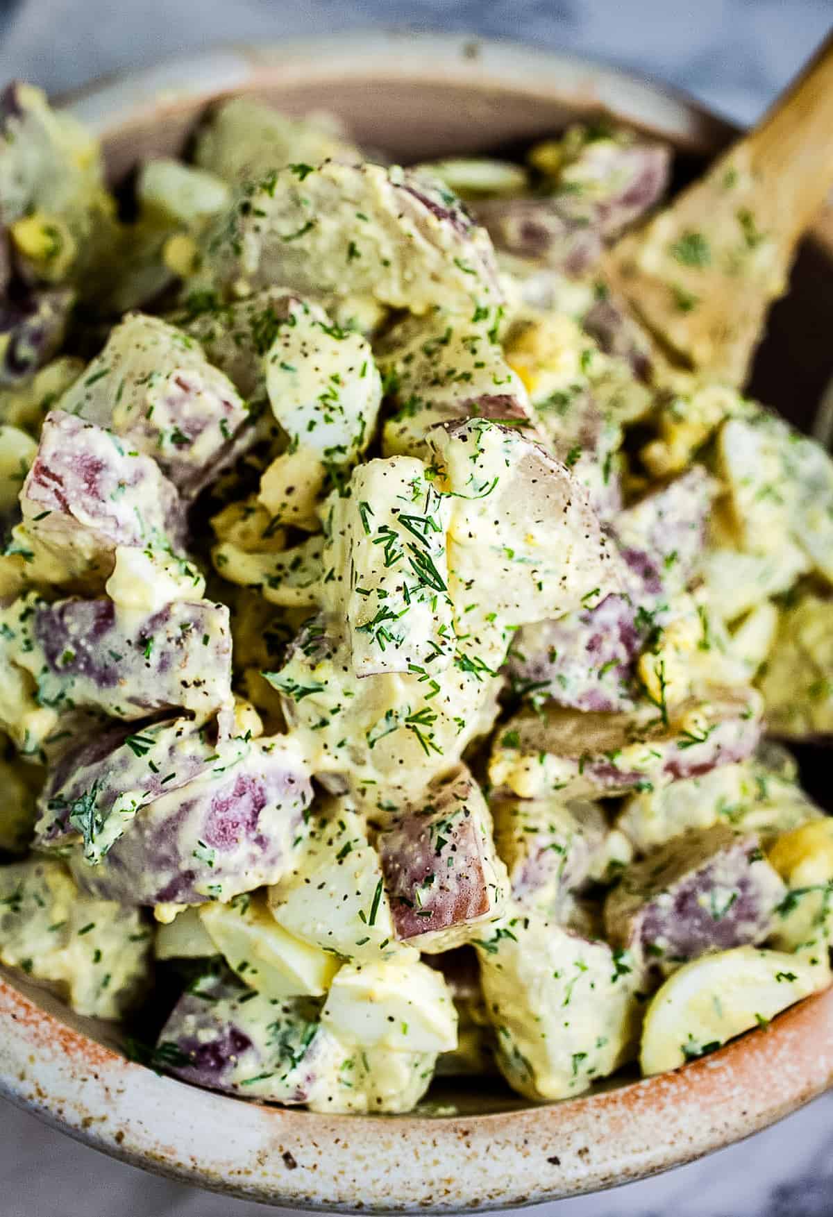 Bowl of Dill Potato Salad with wooden spoon in it