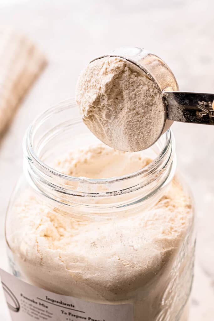 Measuring cup getting pancake mix out of jar