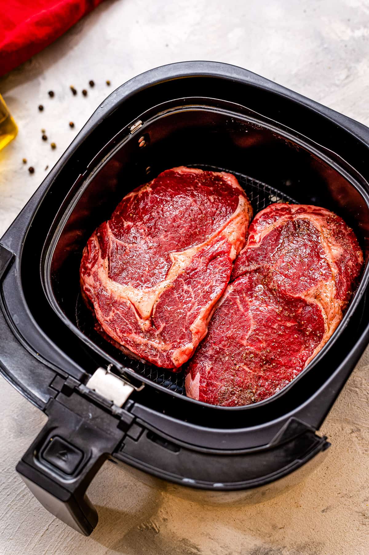 Two raw steaks in an air fryer basket